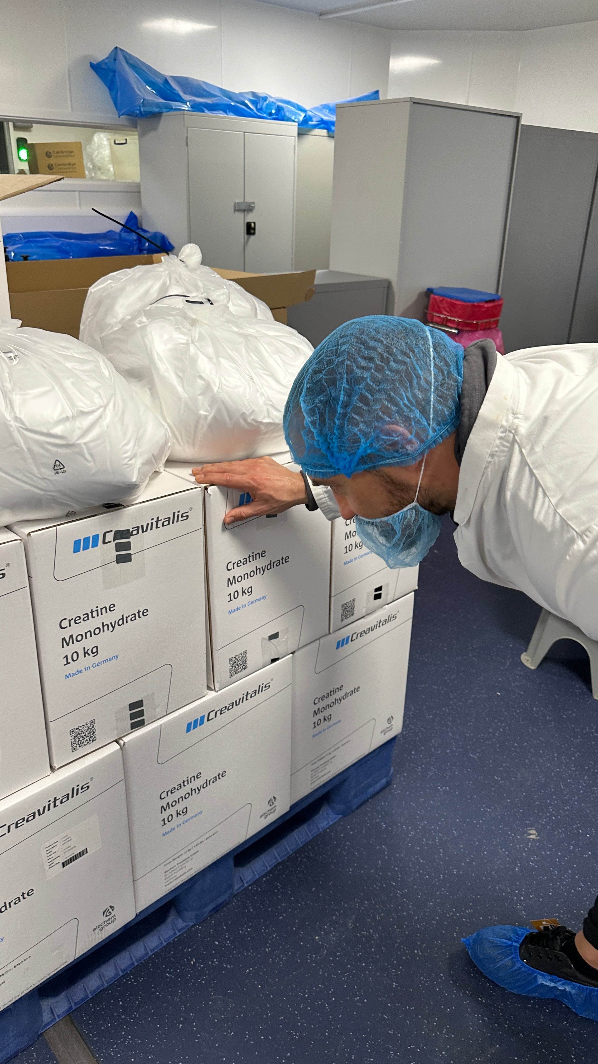 Person in a blue hairnet and white protective clothing inspecting boxes on a pallet.