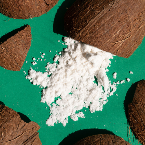 Coconut halves surrounding a pile of white powder on a green surface.